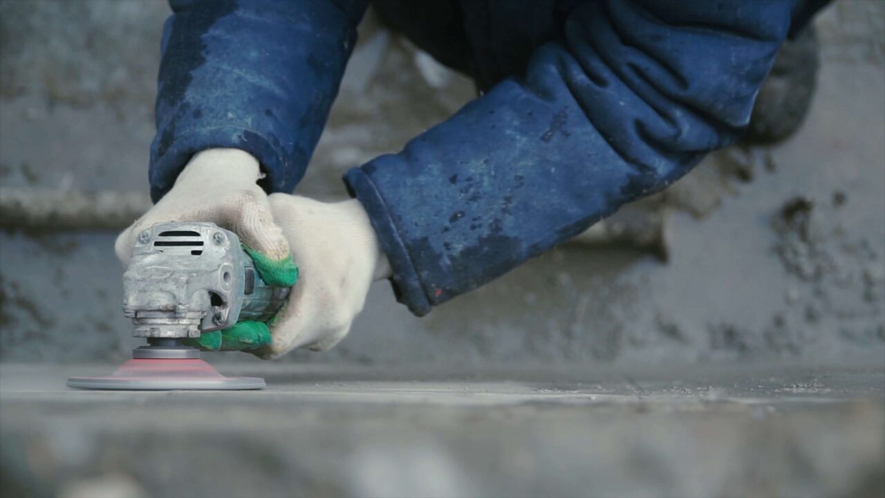 Man using a handheld tool to grind a concrete slab surface.